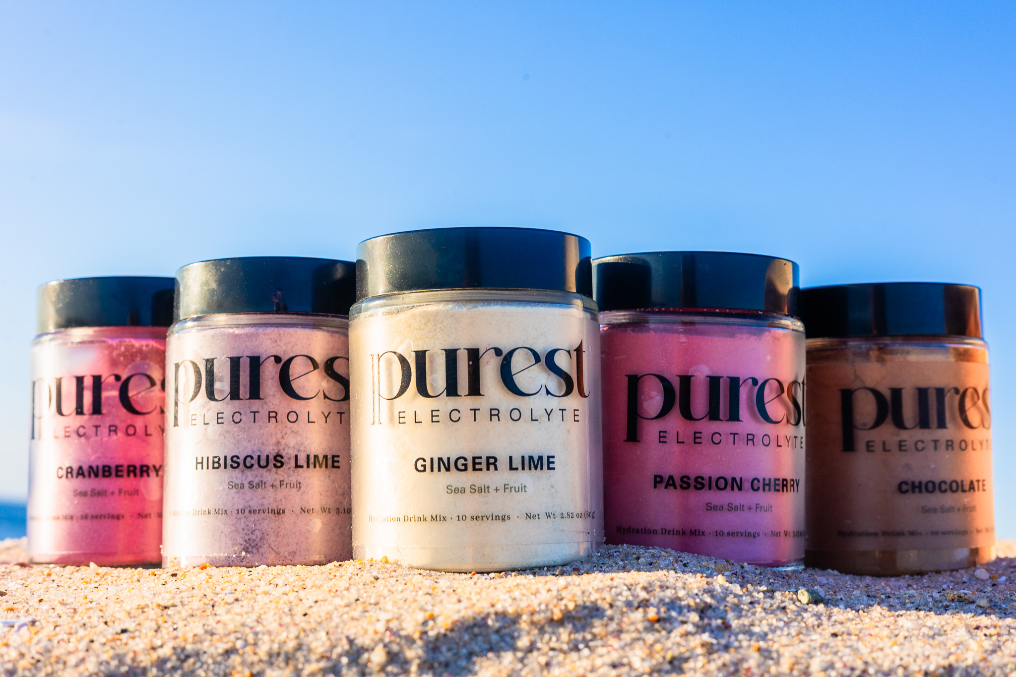 Five flavors of Purest Electrolyte powder in clear glass jars with naturally colored fruit powders visible